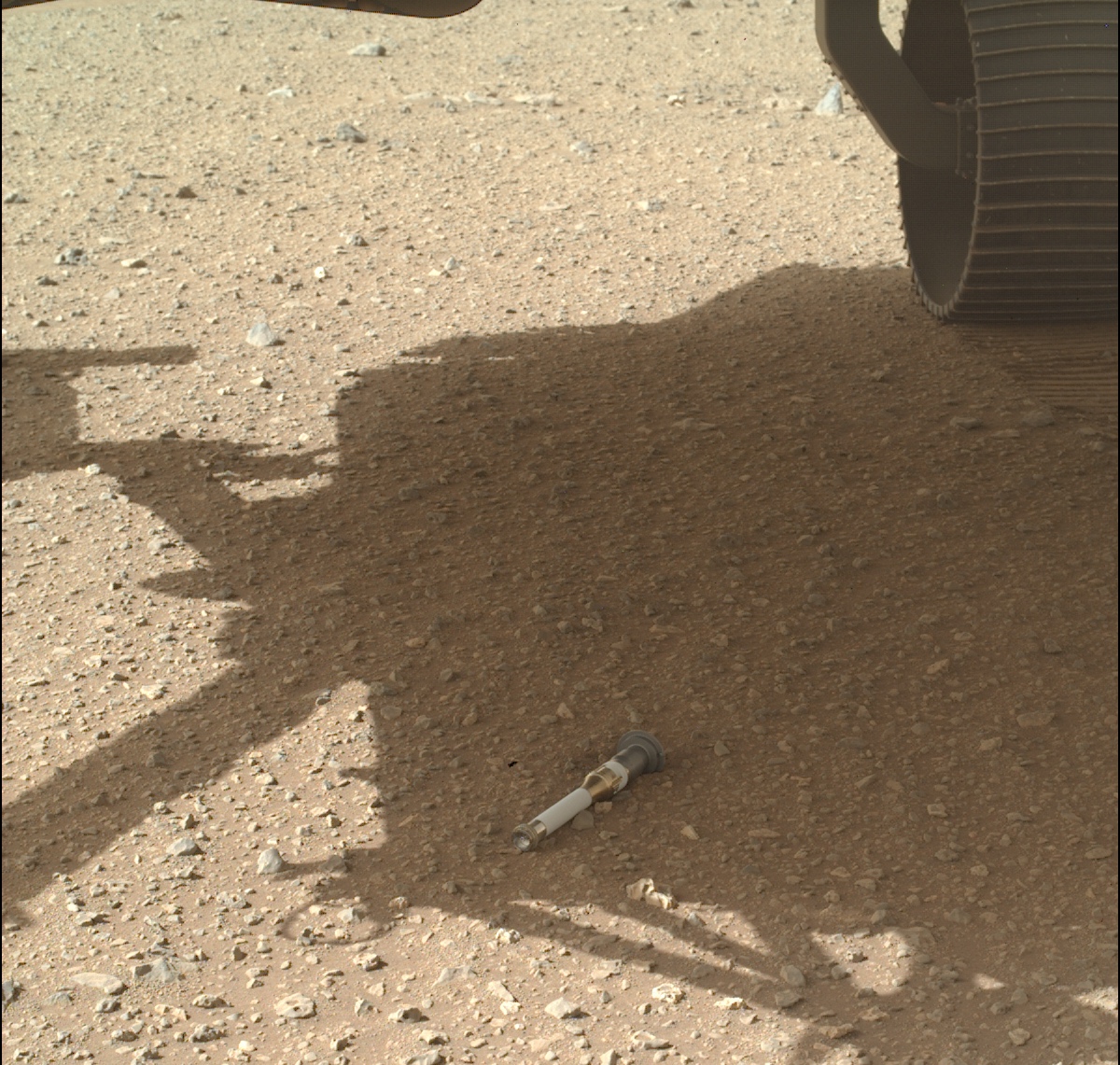 Ein Probenröhrchen auf der Marsoberfläche im Schatten des Rovers Perseverance